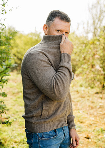 Thorsten L., Gründer von Supplera - Mann in braunem Strickpullover, der draußen vor grünen Büschen steht